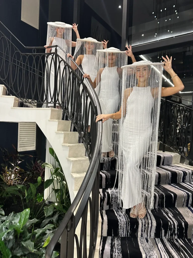 Women wearing white dresses and fringed tassel hats on staircase.
