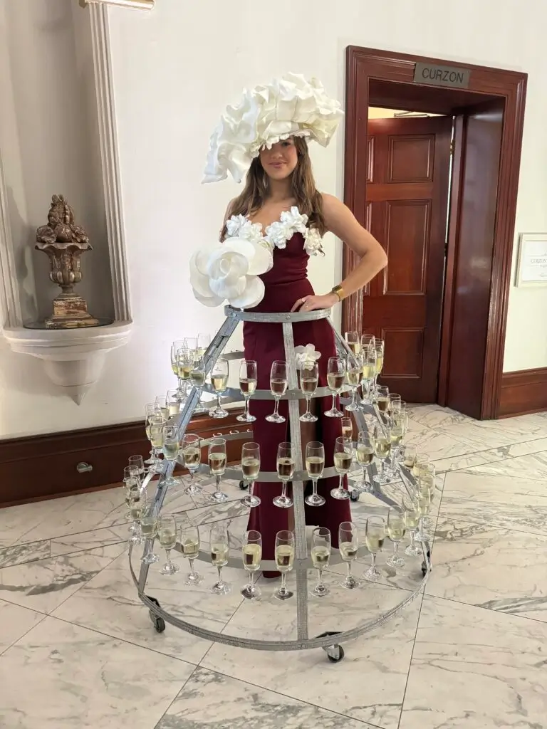 Woman wearing a giant flower hat and champagne glass dress