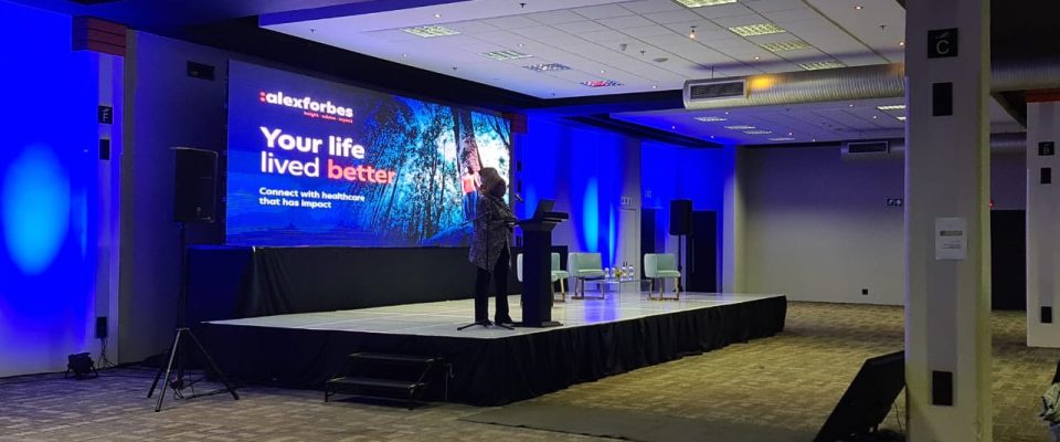 Speaker addressing audience on illuminated corporate event stage