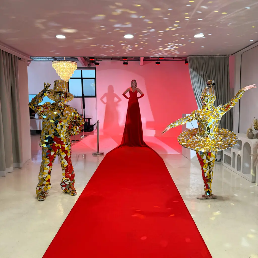 Two gold mirror suit performers standing near red carpet