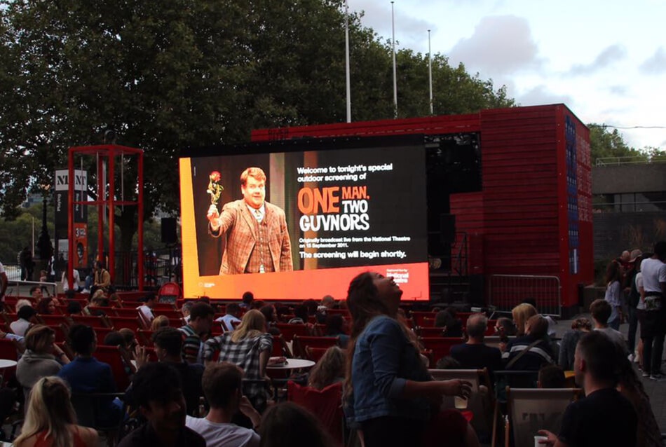 Large outdoor presentation screen displaying speaker at night event