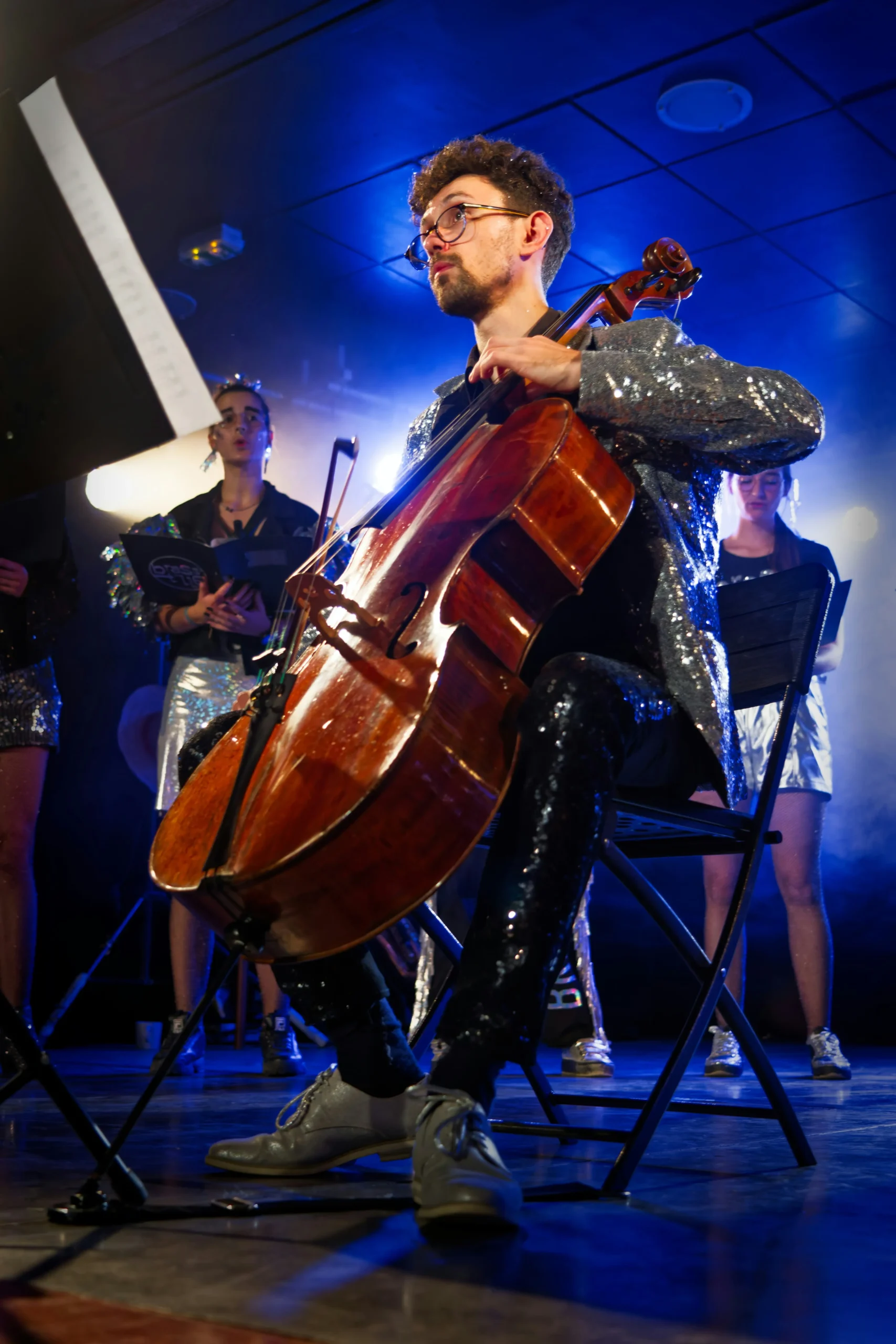 Male musician in jacket performing with cello on stage live.
