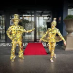 Two gold mirror performers standing near red carpet entrance