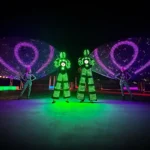 Green LED stilt walkers and dancers performing on stage backdrop