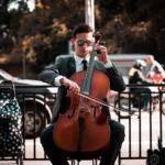 Suited male cellist playing acoustic cello outdoors on city street.