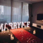 Bed decorated with "MARRY ME" letters and a rose petal heart.