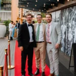 Well-dressed guests posing on red carpet backdrop at event