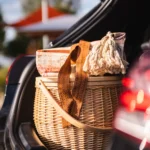 Woven wicker picnic basket with blanket packed inside an open car trunk.