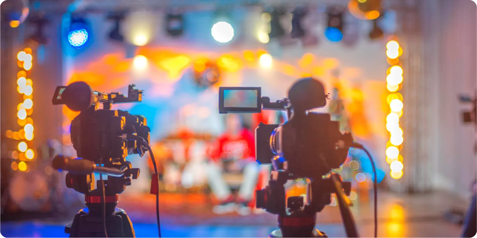 Videographer operating professional camera setup facing blurred colorful stage