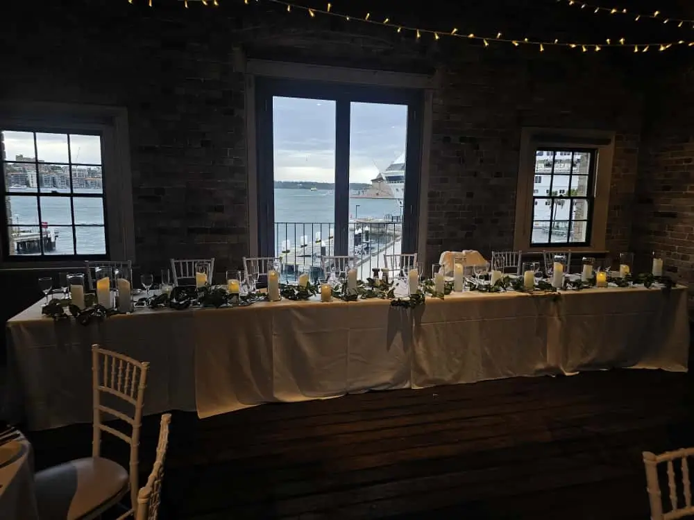 Long wedding head table set up near large window.