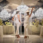 Models wearing white dresses and fringed tassel hats posing indoors.