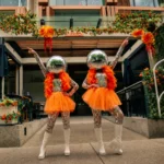 Two disco ball head performers in orange tutus outdoors