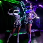 Two disco ball head dancers performing under colorful stage lights