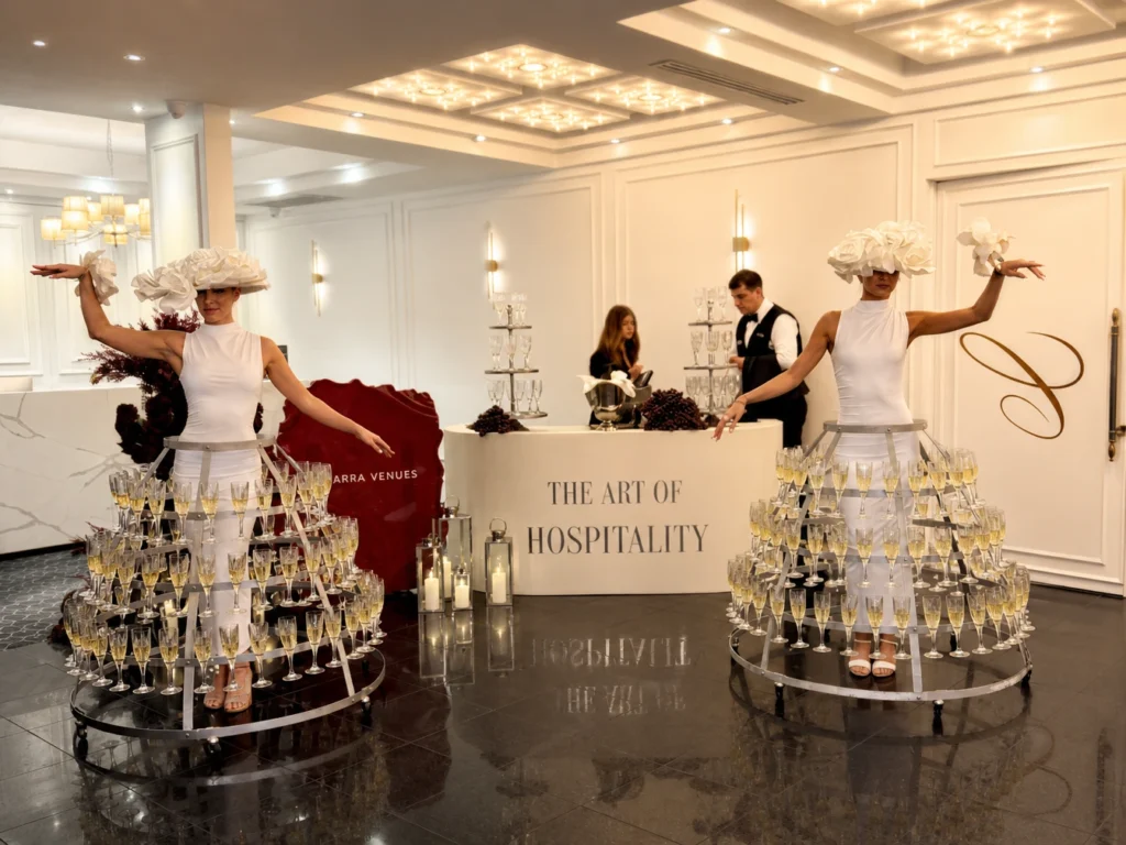 Two women in white outfits wearing metal champagne glass skirts