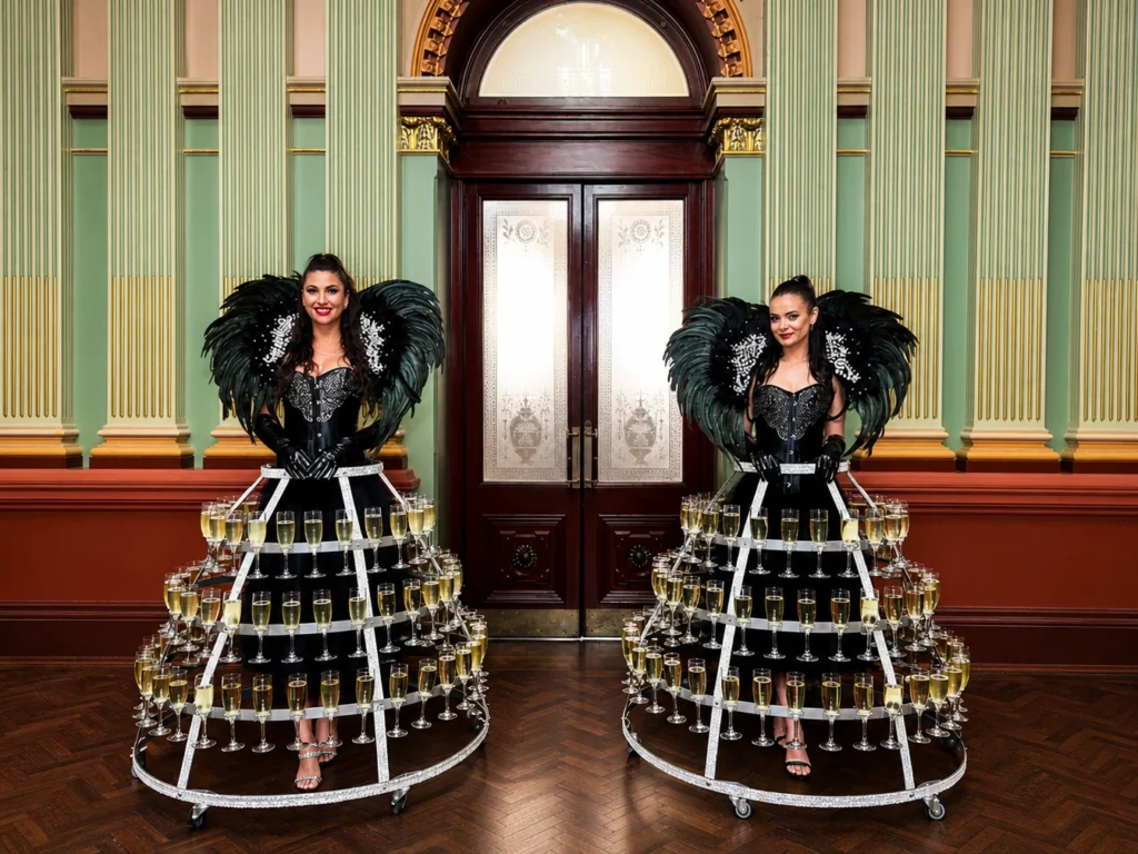 Two women wearing black feathered outfits with champagne glass skirts