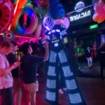 Stilt walker in illuminated LED costume high-fiving party guest