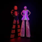 Two performers in red and pink glowing LED stilt suits