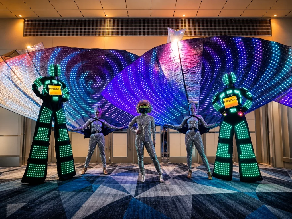 Performers in LED stilt costumes posing against glowing backdrop