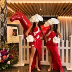 Two women in red dresses with flower headpieces near horse