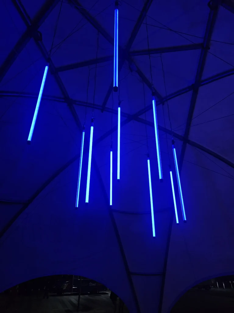 Vertical blue LED light tubes suspended from dark venue ceiling