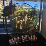Greenery backdrop featuring glowing yellow neon sign at daytime