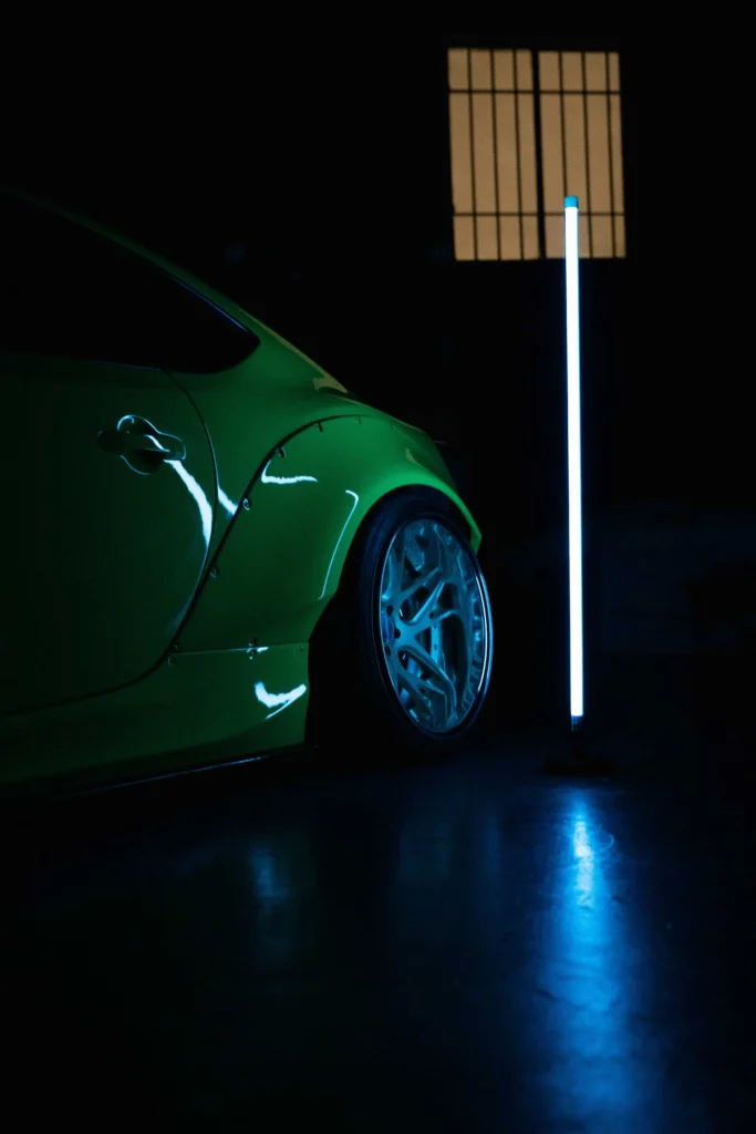 Green car display lit by vertical neon light bar indoors