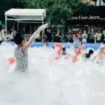 Children playing inside an inflatable pool filled with thick white foam.