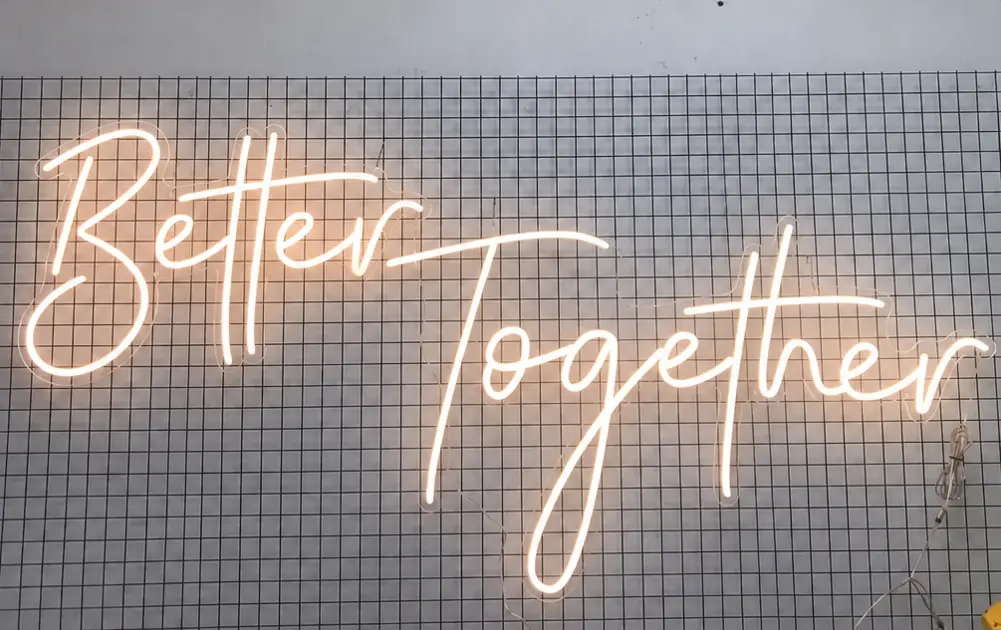 Warm glowing "Better Together" neon sign on grid backdrop