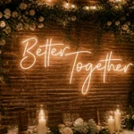 Glowing "Better Together" neon sign mounted against lush foliage wall