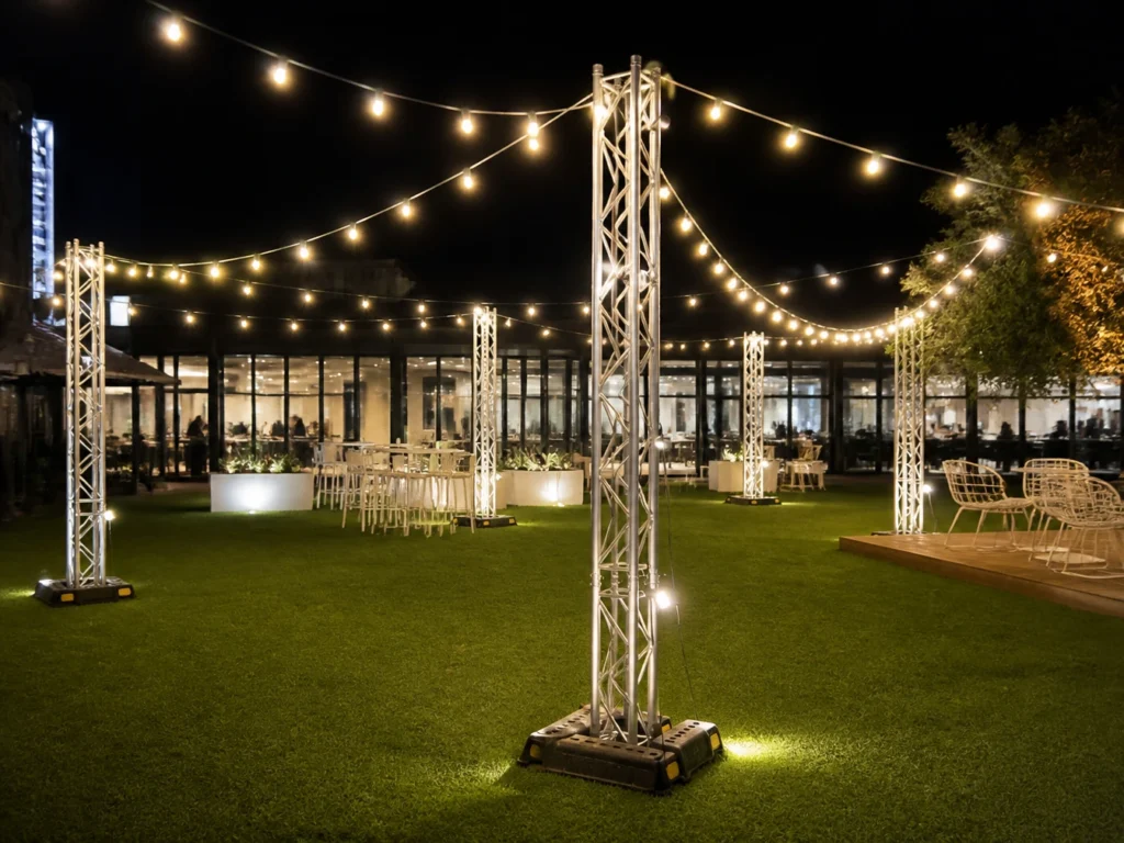 Outdoor event space decorated with hanging string fairy lights on truss posts.