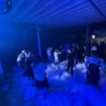 Crowded nighttime foam party illuminated by blue lighting with people dancing.