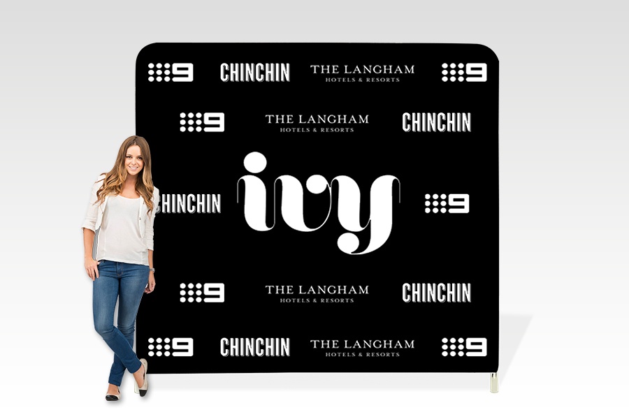 Woman posing beside black media backdrop wall printed with logo