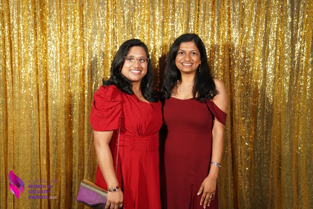 Two women posing smiling in front of gold sequin backdrop