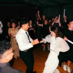Bride and groom dancing happily with guests at a wedding reception.