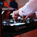 Close-up of a DJ using a mixing console and laptop.