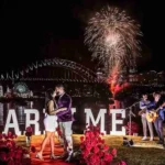 Couple embracing by MARRY ME letters with fireworks and live band in Sydney.