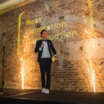 Presenter speaking on stage flanked by bright cold spark