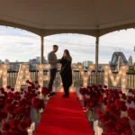 Couple inside a gazebo filled with red roses and MARRY ME letters.