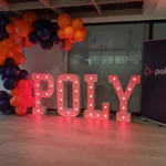 Red marquee letters spelling POLY with orange balloon arch