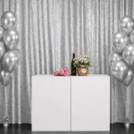 Silver metallic drape backdrop set up with white table and balloon decor.