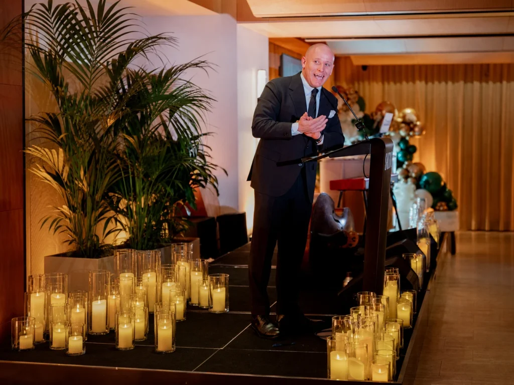 Speaker presenting at podium in front of indoor plant decor.