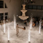 Couple dancing under a crystal chandelier surrounded by dry ice fog and spark fountains.